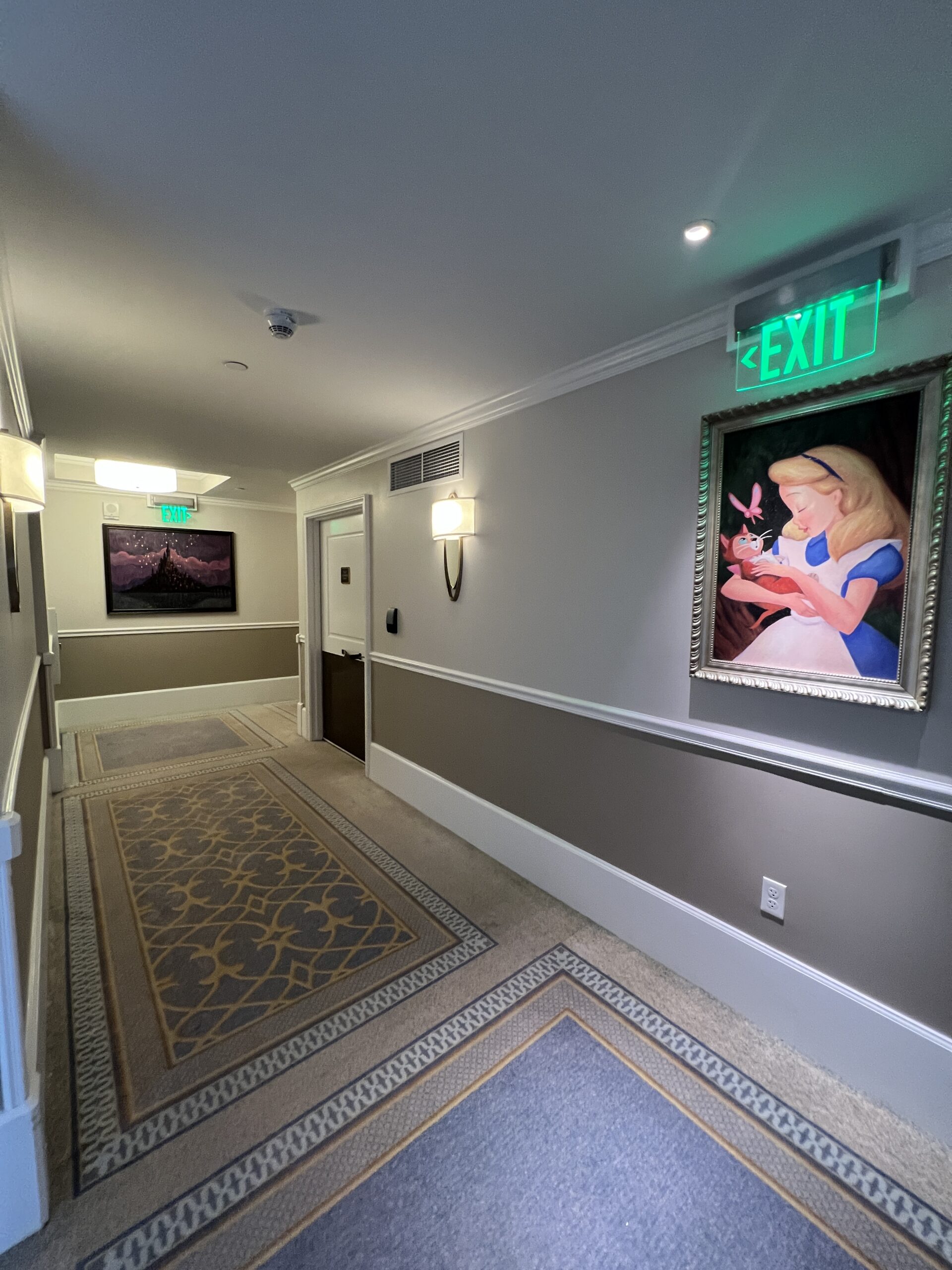 ディズニー・リビエラ・リゾート客室フロアの廊下とアリスの絵画、EXIT サインのある落ち着いた雰囲気の内装