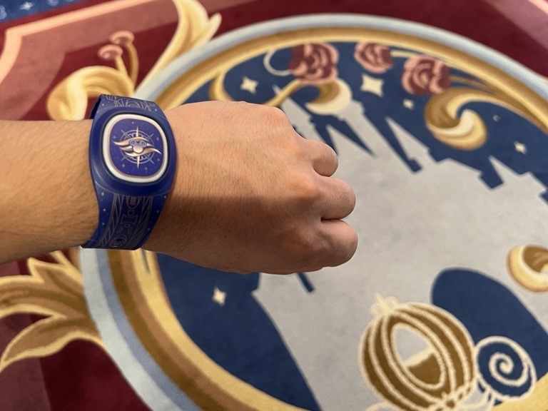 ディズニー・クルーズライン船内で、ディズニーバンド+を手首につけている様子。船内のカーペットを背景にした利用イメージ。